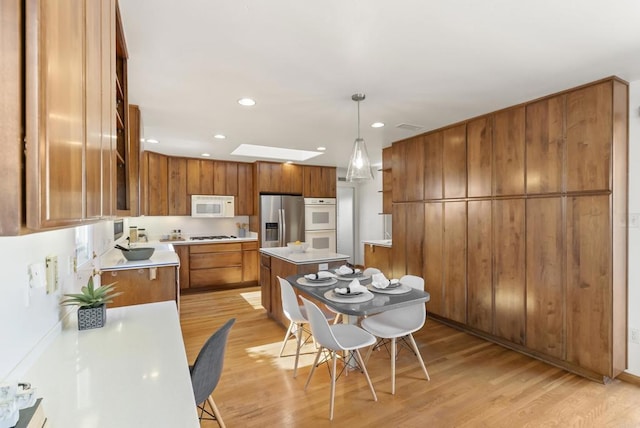 kitchen with white appliances, brown cabinetry, a skylight, light countertops, and light wood-type flooring