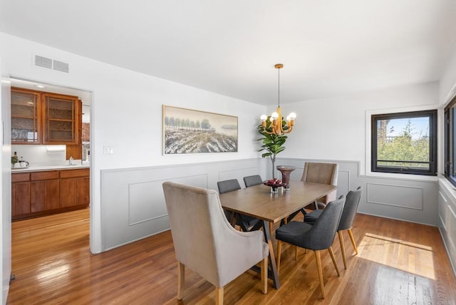 dining space with visible vents, wainscoting, a decorative wall, and light wood-style floors