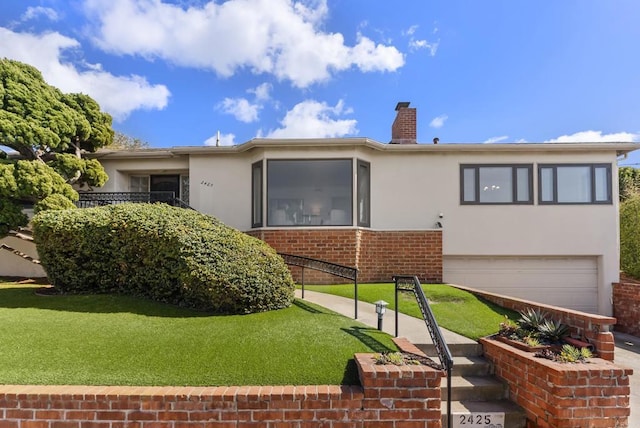 back of property with a yard, an attached garage, a chimney, stucco siding, and brick siding