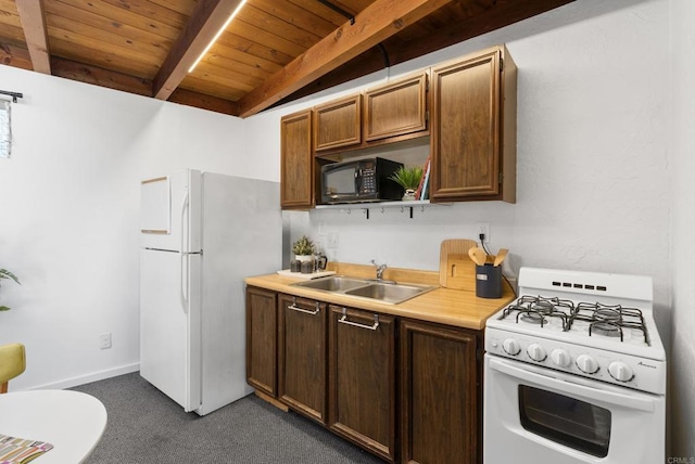 kitchen with white appliances, beam ceiling, a sink, light countertops, and dark carpet