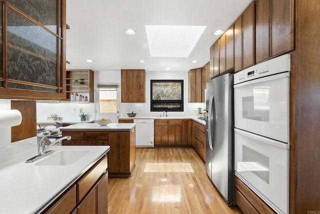 kitchen featuring light wood finished floors, light countertops, a skylight, white appliances, and a sink