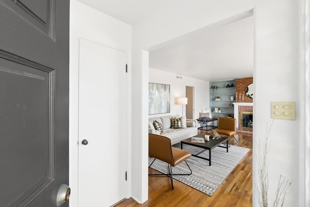 living room featuring built in features, light wood-style floors, and a brick fireplace