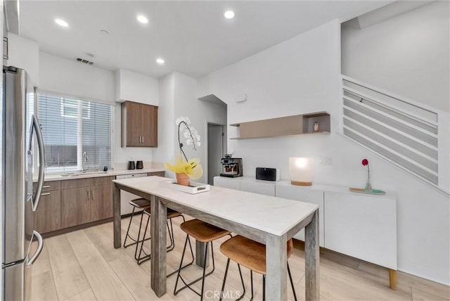 kitchen with stainless steel fridge with ice dispenser, light countertops, light wood-type flooring, dishwashing machine, and a sink