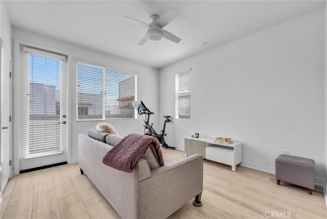 living area featuring baseboards, light wood-type flooring, and ceiling fan