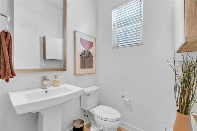 half bath featuring toilet, baseboards, and a sink