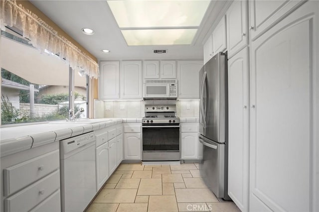 kitchen with tile counters, white cabinets, appliances with stainless steel finishes, and a sink