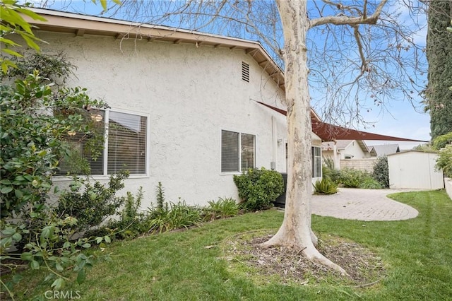 view of side of home with a shed, stucco siding, a lawn, an outdoor structure, and a patio