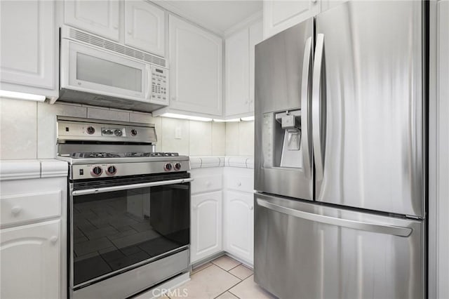 kitchen featuring tile countertops, appliances with stainless steel finishes, light tile patterned flooring, and white cabinetry