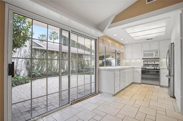 kitchen featuring tile countertops, stainless steel appliances, white cabinetry, and vaulted ceiling