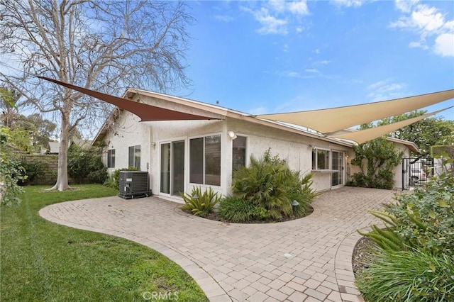 rear view of house featuring a patio area, a yard, central AC unit, and stucco siding