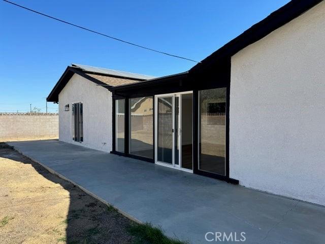 view of property exterior featuring solar panels, a patio area, fence, and stucco siding