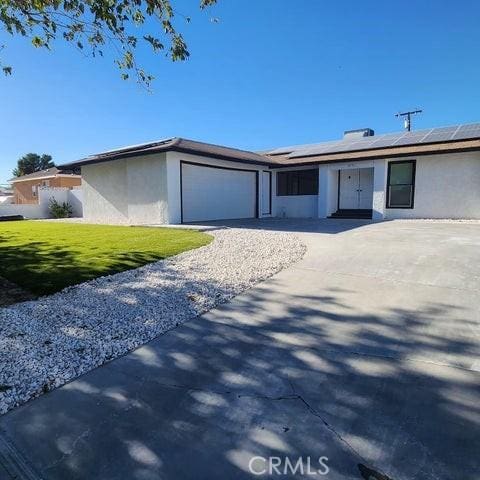 single story home featuring stucco siding, a garage, solar panels, and driveway