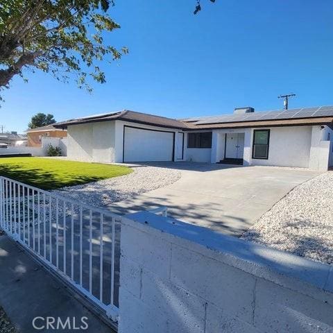 ranch-style house with solar panels, an attached garage, fence, and stucco siding