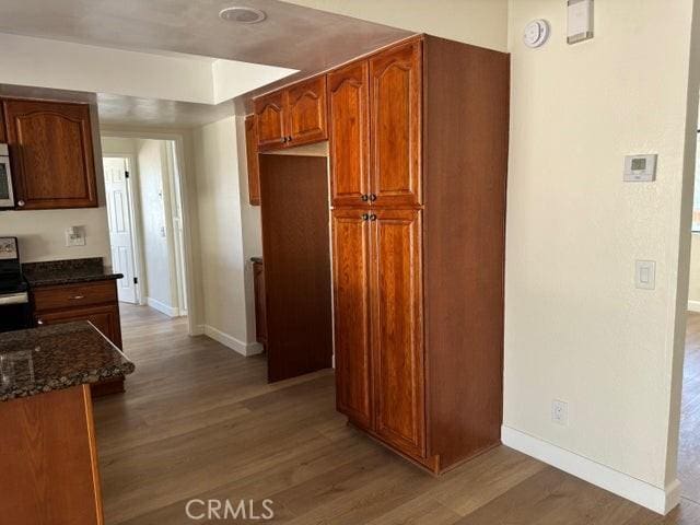 kitchen with baseboards, stainless steel appliances, dark stone counters, and wood finished floors