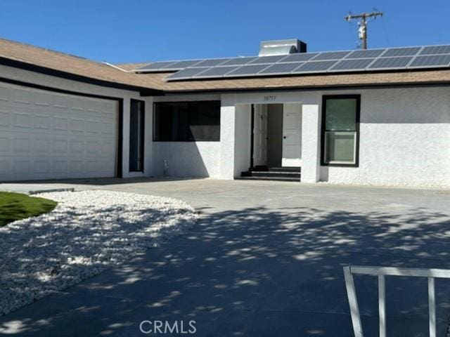 view of front of house featuring an attached garage, driveway, roof mounted solar panels, and stucco siding