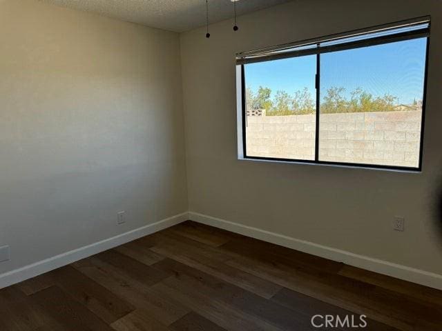 empty room featuring a textured ceiling, baseboards, and dark wood-style flooring