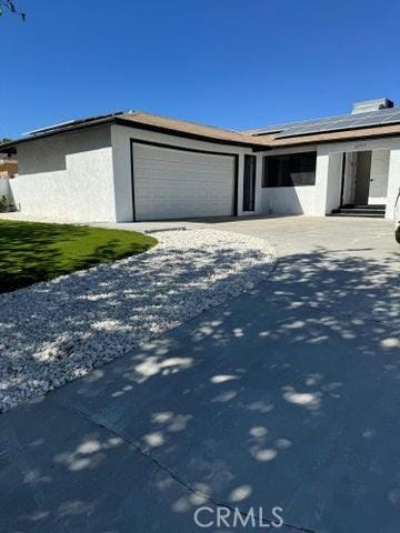 view of front of property with stucco siding, an attached garage, solar panels, and driveway