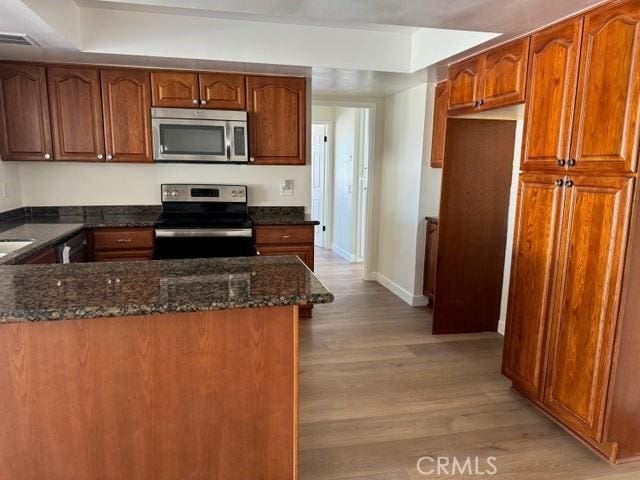 kitchen with dark stone counters, light wood-style flooring, brown cabinetry, and appliances with stainless steel finishes