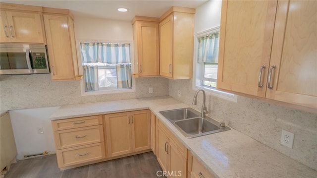 kitchen with a sink, stainless steel microwave, tasteful backsplash, and light brown cabinetry