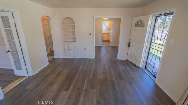 interior space with built in features, baseboards, dark wood-type flooring, and arched walkways