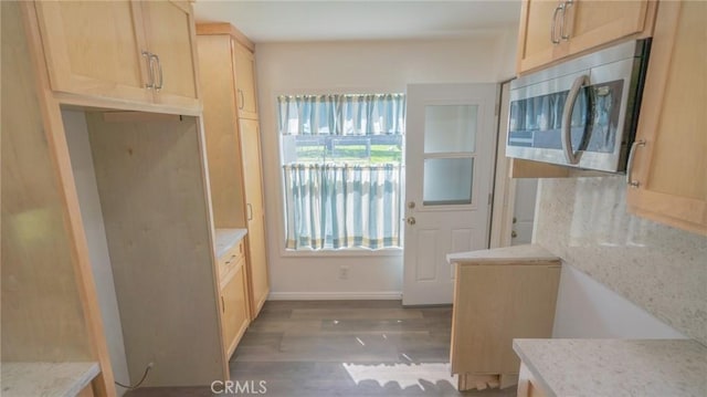 kitchen with light brown cabinetry, stainless steel microwave, wood finished floors, baseboards, and light stone countertops