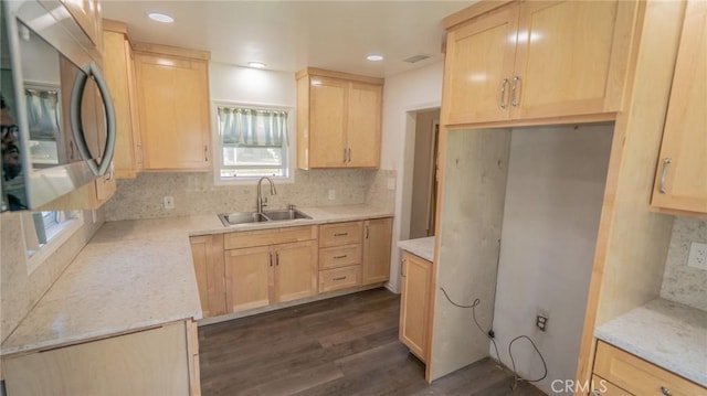 kitchen with a sink, stainless steel microwave, backsplash, and light brown cabinetry