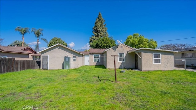 rear view of house with stucco siding, a lawn, and fence