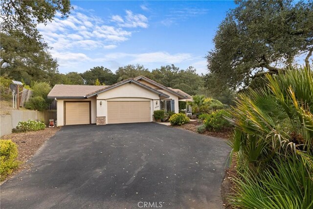 single story home with fence, an attached garage, stucco siding, a tile roof, and aphalt driveway