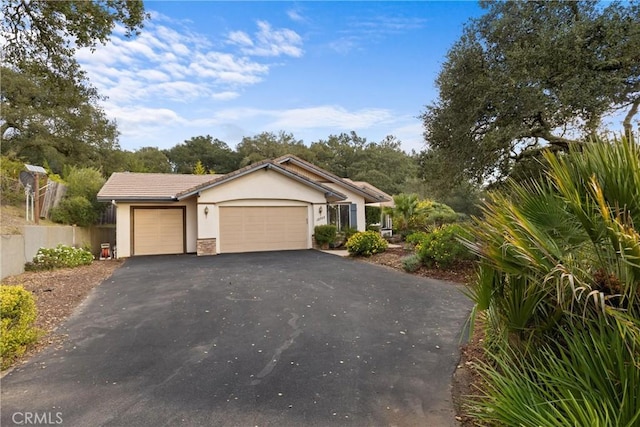 view of front facade with an attached garage, a tiled roof, driveway, and stucco siding
