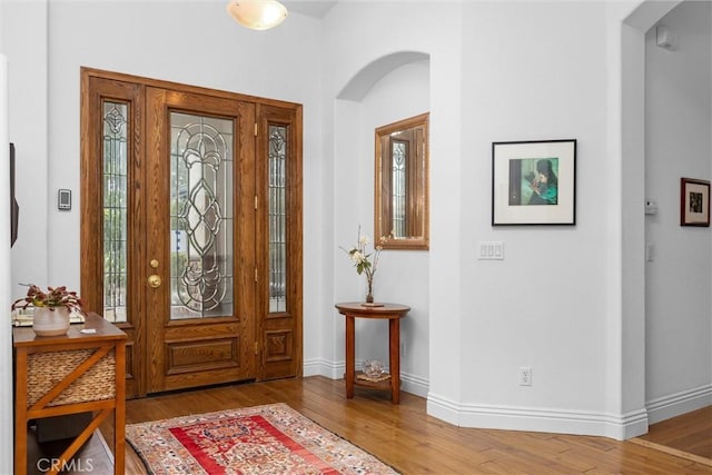 foyer entrance featuring a wealth of natural light, arched walkways, wood finished floors, and baseboards