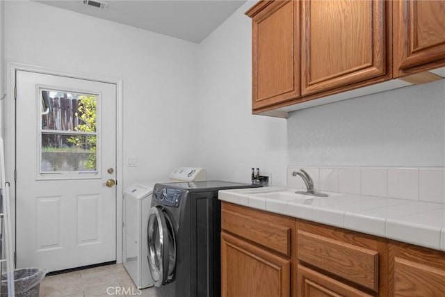 washroom featuring washing machine and clothes dryer, light tile patterned flooring, a sink, and cabinet space