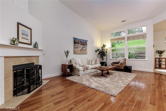 living area featuring a tiled fireplace, baseboards, visible vents, high vaulted ceiling, and wood-type flooring