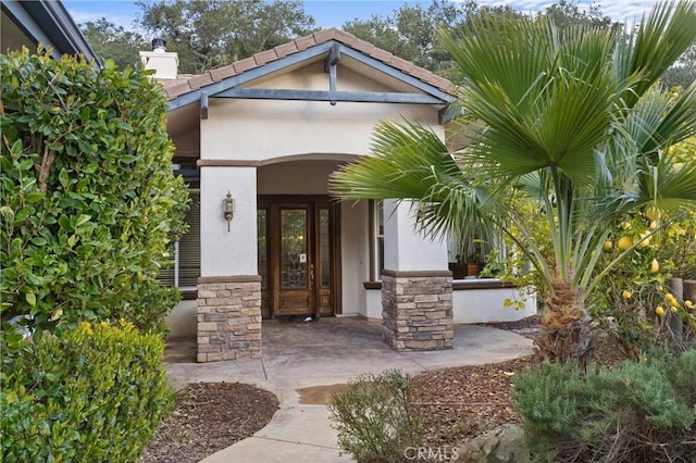 view of exterior entry with stucco siding, stone siding, and a chimney