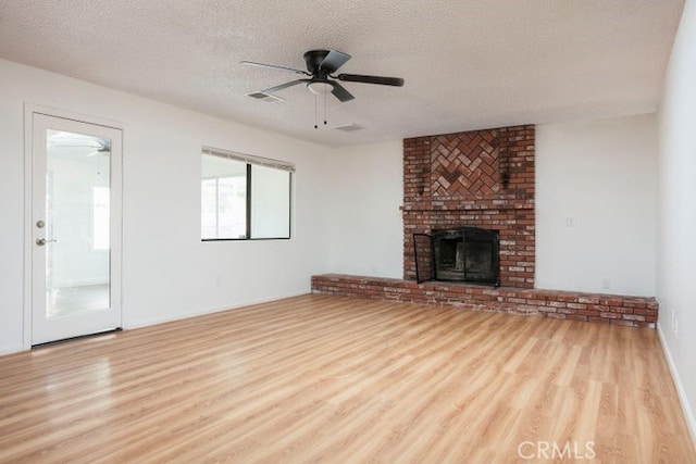 unfurnished living room with ceiling fan, a textured ceiling, a brick fireplace, and wood finished floors