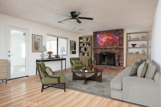 living room featuring a ceiling fan, a textured ceiling, wood finished floors, and a fireplace