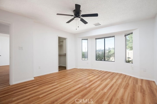 unfurnished bedroom with visible vents, a textured ceiling, a walk in closet, and light wood-style floors