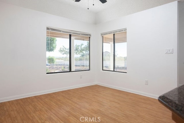 spare room featuring ceiling fan, light wood-style flooring, baseboards, and a textured ceiling