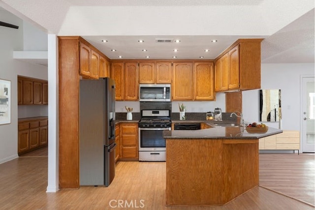 kitchen with brown cabinets, a peninsula, a sink, stainless steel appliances, and light wood-type flooring