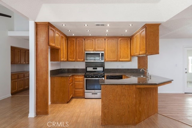 kitchen with dark countertops, light wood-style flooring, appliances with stainless steel finishes, a peninsula, and a sink