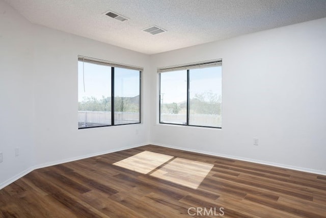 unfurnished room featuring a textured ceiling, wood finished floors, visible vents, and baseboards