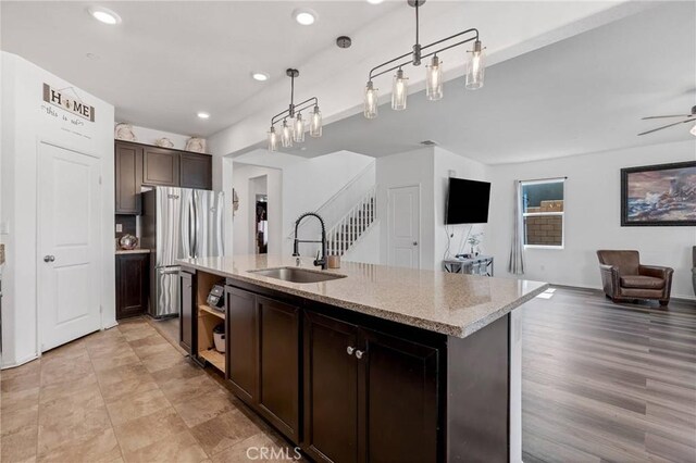 kitchen with dark brown cabinets, open floor plan, pendant lighting, freestanding refrigerator, and a sink