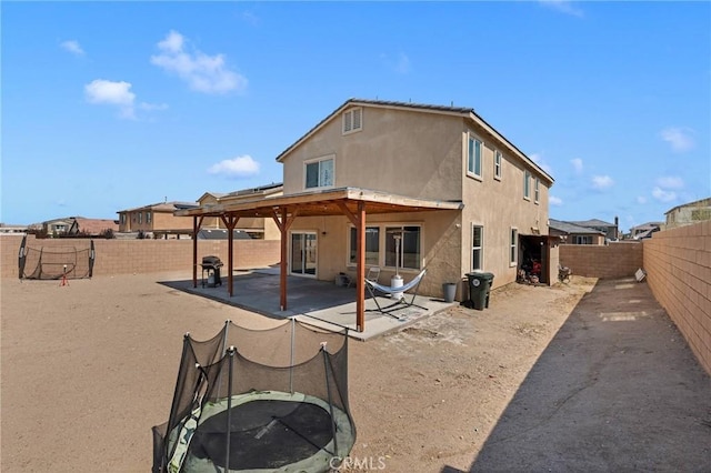 back of property with a patio, a trampoline, a fenced backyard, and stucco siding