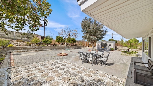 view of patio featuring a fenced backyard, a shed, a fire pit, an outdoor structure, and outdoor dining area