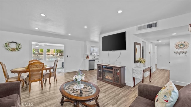 living room with recessed lighting, visible vents, light wood-style floors, and a glass covered fireplace