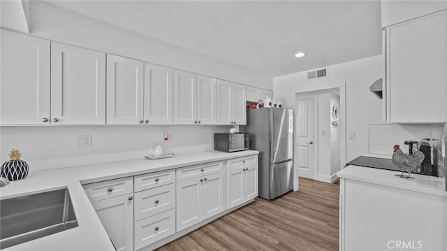 kitchen featuring visible vents, black microwave, freestanding refrigerator, white cabinetry, and a sink