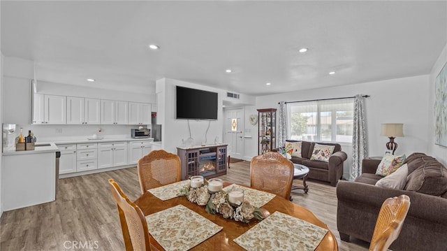 dining area featuring a glass covered fireplace, light wood-style flooring, recessed lighting, and visible vents