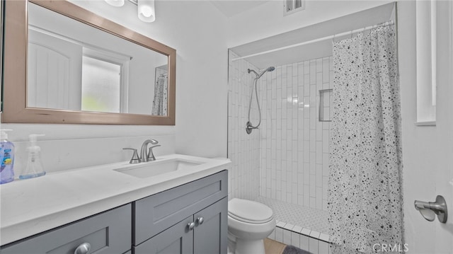 full bath with vanity, toilet, visible vents, and a tile shower