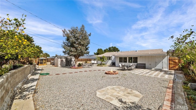 rear view of house with an outdoor fire pit, a storage shed, a fenced backyard, an outbuilding, and a patio