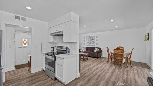 kitchen featuring under cabinet range hood, tasteful backsplash, wood finished floors, stainless steel range with electric cooktop, and light countertops