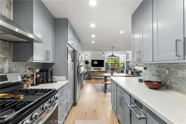 kitchen featuring appliances with stainless steel finishes, wall chimney exhaust hood, gray cabinetry, and light countertops